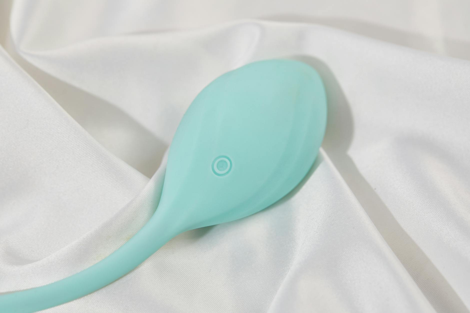 A stylish teal vibrator on smooth white silk fabric, perfect for adult lifestyle imagery