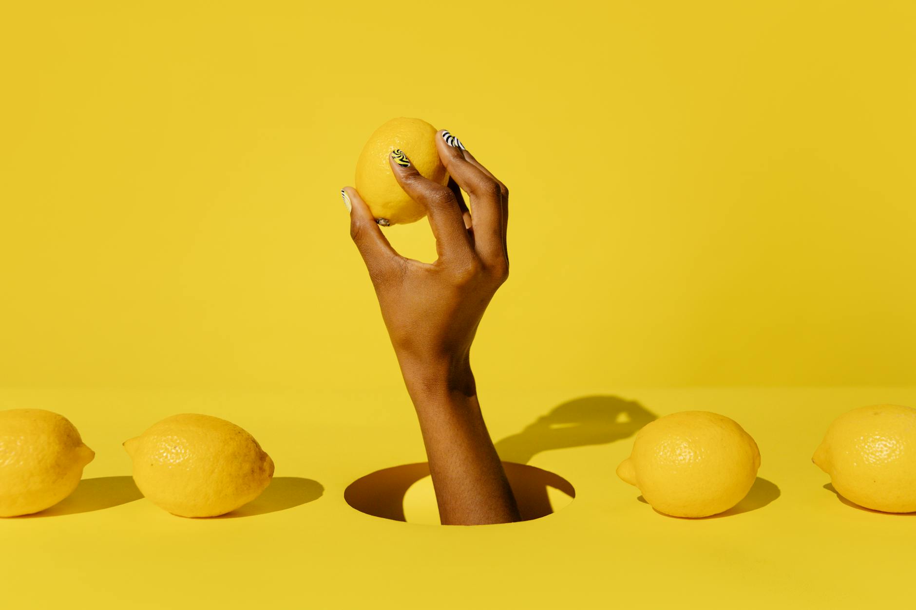 A hand holding a fresh lemon against a vivid yellow background, symbolizing the bright sensation of lemon clitoral vibrators
