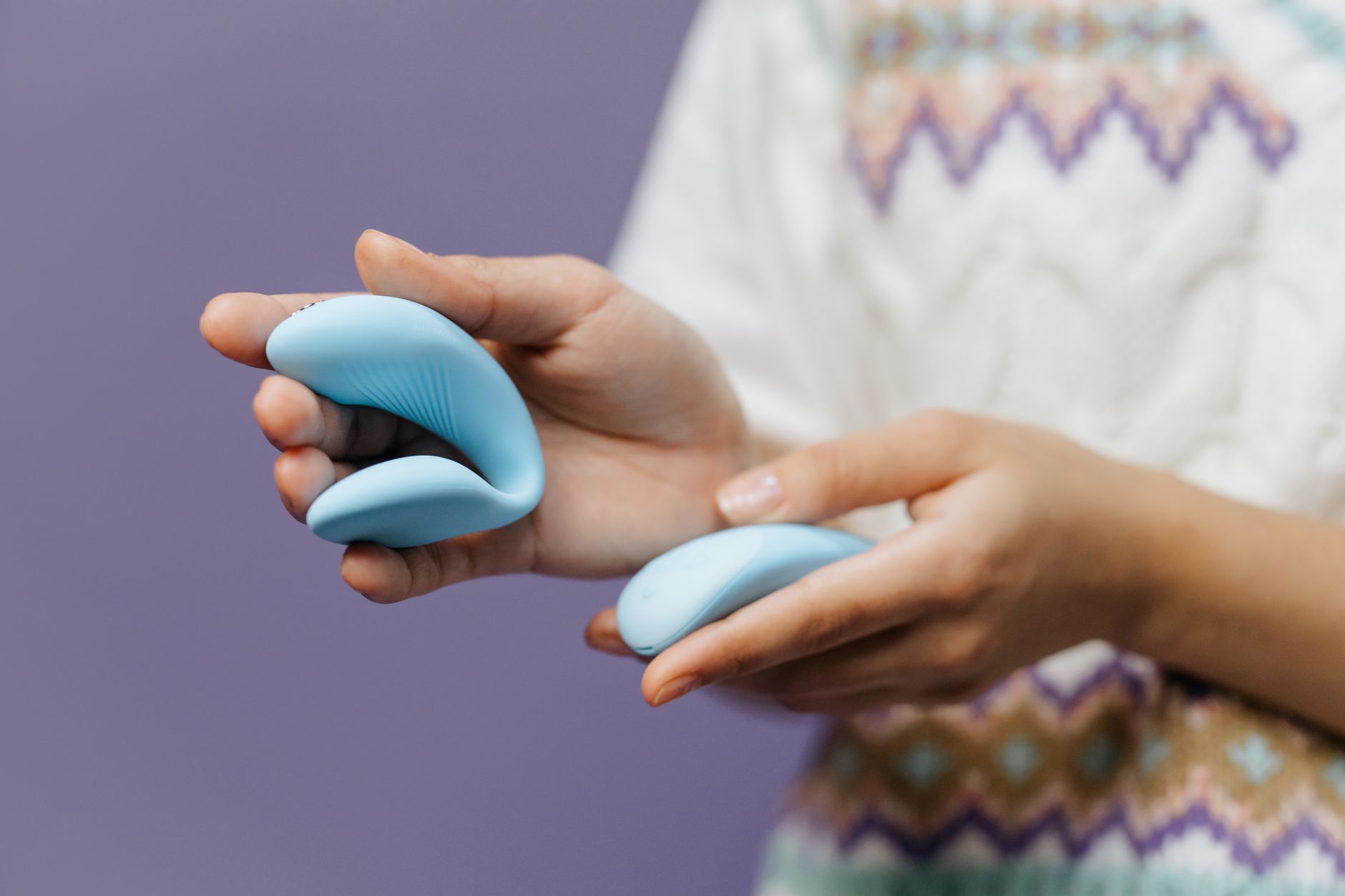 Close-up of hands holding a sleek blue lemon clitoral vibrator against a purple background