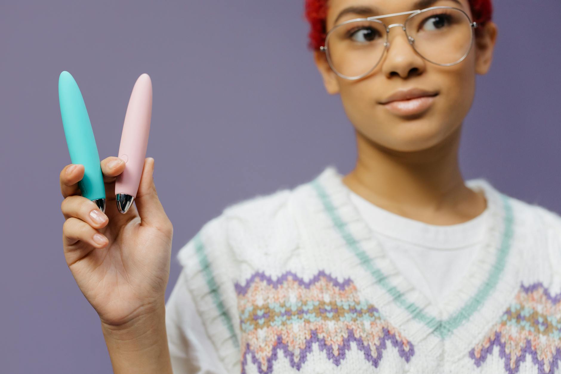 Mujer joven sosteniendo dos vibradores de colores contra fondo púrpura durante exploración de placer