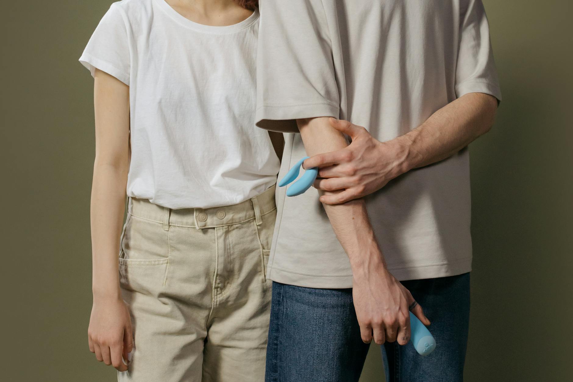 A young couple standing together indoors, holding a vibrator and exploring pleasure together