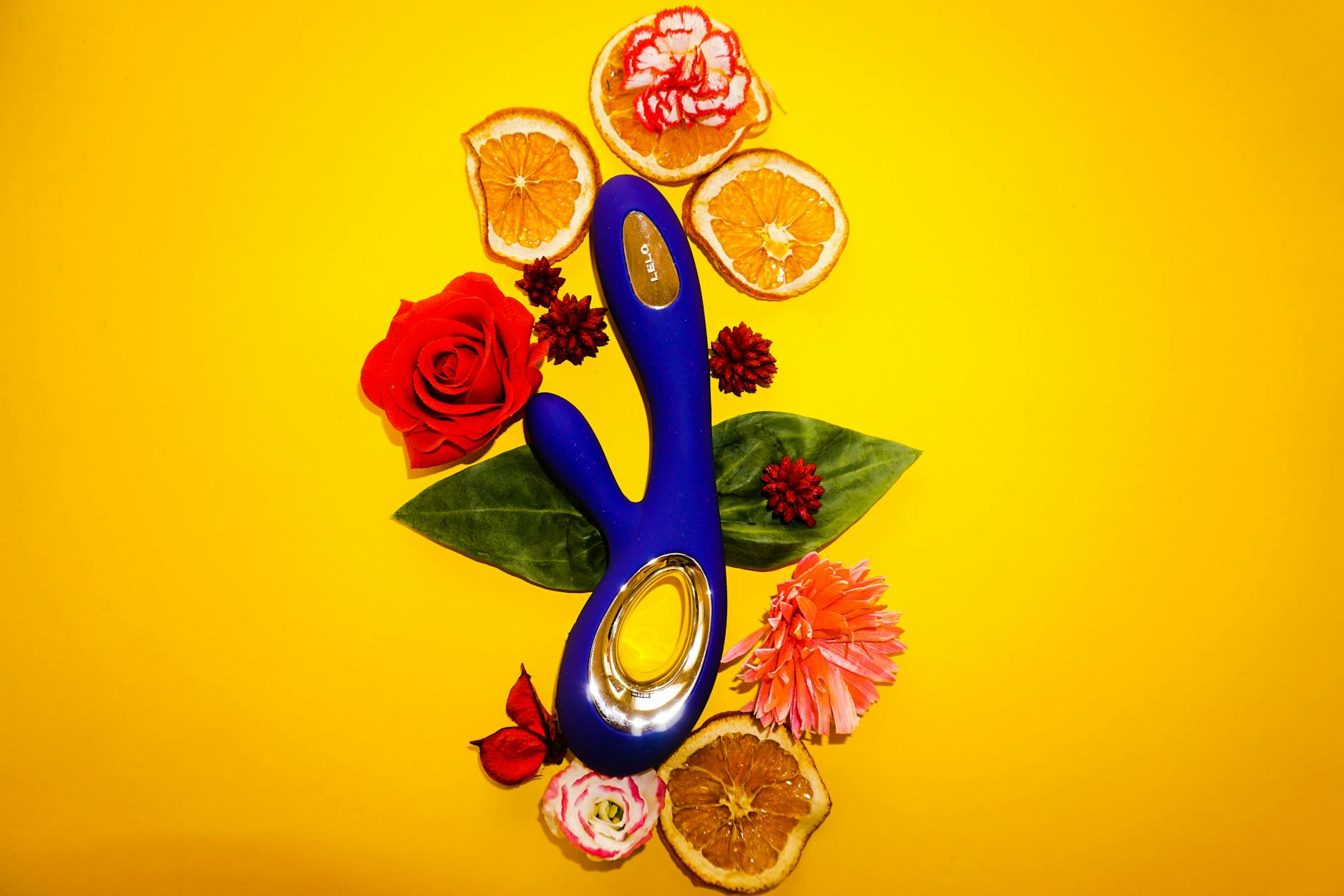 Blue lemon vibrator surrounded by fresh flowers and citrus slices on a bright yellow background